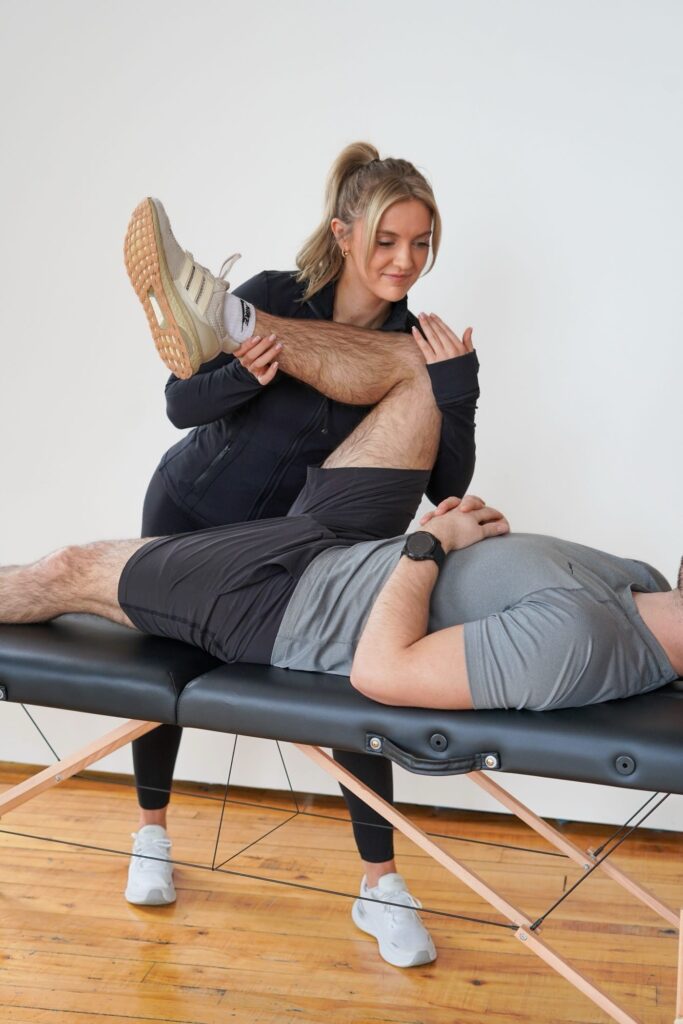 Sam performing physical therapy exercises on a man lying on a treatment table.