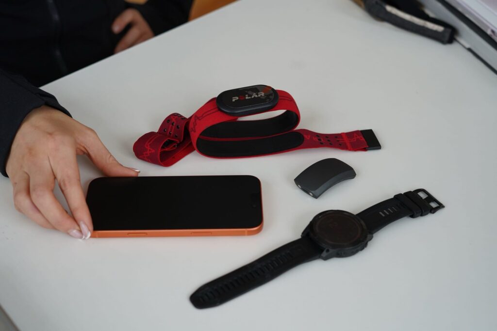 A wearable fitness tracker, smartwatch, and smartphone on a white table.