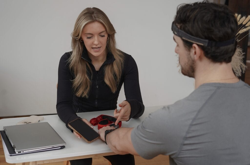 A woman assisting a man with fitness training and wearable device setup.