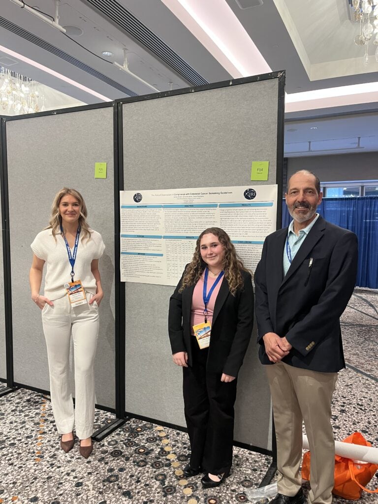 A woman, a girl, and a man standing in front of a research poster at an academic conference.